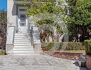 A yard with lemon trees and marble stairs to a vintage family house entrance with a white door.