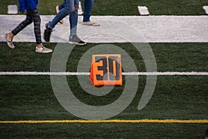 30 yard line marker on football field as feet and legs of teenagers walk past on field