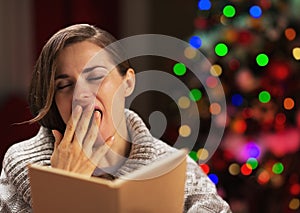 Yawing young woman with book in front of christmas tree photo