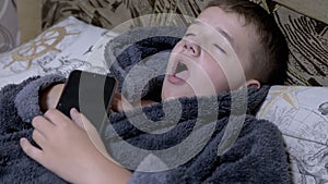 Yawning Child in Home Gray Dressing Gown Falls asleep with Smartphone in Hands