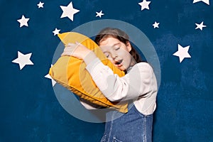Yawning little girl with eyes closed hugging yellow comfortable pillow