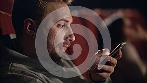 Yawning man using smartphone in cinema. Young man watching boring film