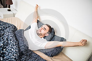 Yawning and stretching man waking in bed at home