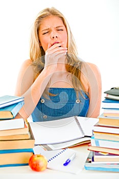 Yawning teen girl sitting at table with books