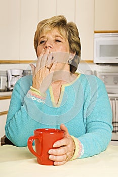 Yawning woman with red coffee mug in her kitchen