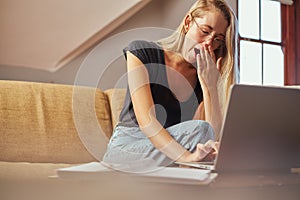 Yawning young woman working from home on sofa