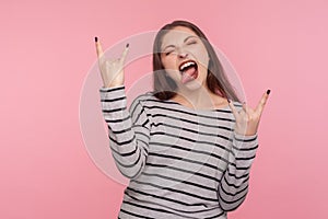 Yeah, awesome ! Portrait of excited rocker woman in striped sweatshirt showing rock and roll hand gesture