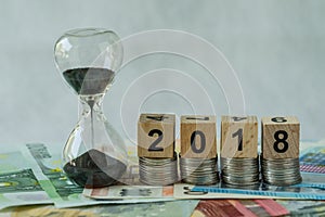 Year 2018 business time countdown or long term investment concept as hourglass or sandglass on pile of Euro banknotes with wooden