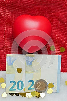 Year 2022 made out of Euro bank notes and coin. On red Santa hat and golden heart shape confetti. New year celebration and change