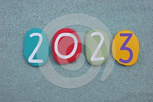 Year 2023 composed with multi colored stone numbers over green sand