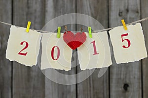 Year 2015 antique paper sign with red heart hanging from clothesline by wood fence