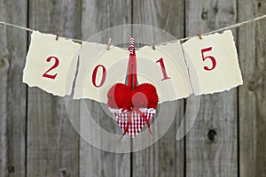 Year 2015 on antique parchment paper hanging on clothesline with red heart by wooden background