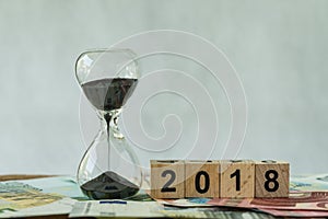 Year 2018 business time countdown or long term investment concept as hourglass or sandglass on pile of Euro banknotes with wooden