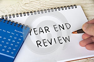 Year end review text on notepad with December calendar on wooden table. Year end review concept.