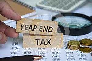 Year end tax text on wooden block with pen, notepad, calculator and coins background. Tax assessment concept