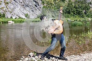 23 year guy with beard in black shirt and sunglasses holds steaming guitar. musician with smoking guitar in open air photo