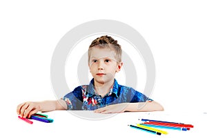 A 6 year old boy in a blue shirt paints with pencils on a white background isolate