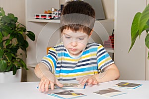 A 4-year-old boy puts together a picture of a raccoon from puzzles while sitting at the table.