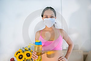 A 20-year-old brunette woman wearing a mask in sportswear rejoicing and drinking water after training