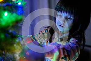 A 4-year-old charming little girl decorates a Christmas tree in light of garlands