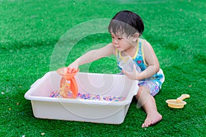 2 year old child boy is playing colorful water beads in white basin.