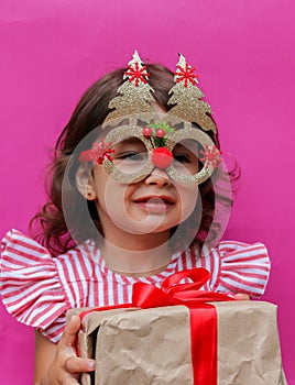 A 3-year-old girl in a red and white dress with a gift in her hands. The gift is packed in kraft paper with a red ribbon