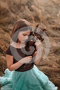 A 10-year-old girl is walking in a field. Dry grass all around. The girl is holding a bouquet.