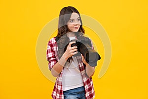 12, 13, 14 year old teen girl holding digital camera or DSLR over yellow background.