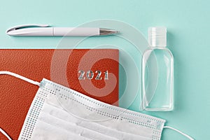 2021 year red leather diary  pen  small bottle of hand sanitizer and disposable medical face mask on a pale turquoise backgriound photo
