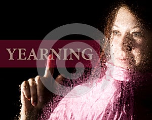 Yearning written on virtual screen. young woman melancholy and sad at the window in the rain, her neck warm scarf