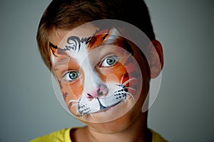 Years old boy with blue eyes face painting of a cat or tiger. Orange.