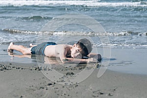 13 years old boy relaxation on the sand on the beach in the sea waves. Concept of family summer vacation