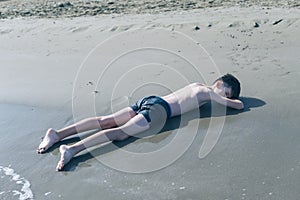 13 years old boy relaxation on the sand on the beach in the sea waves. Concept of family summer vacation