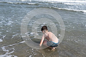 13 years old boy relaxation on the sand on the beach in the sea waves. Concept of family summer vacation