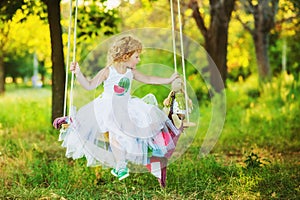 3 years old girl in green sneakers, white ballerinas skirt and white watermelon printed t-shirt swinging in garden with her toy.