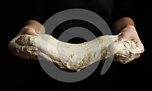 Yeast dough on a black background in the hands of a cook