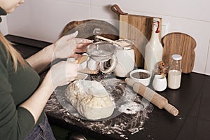 Yeast dough ready for making homemade buns is on the table among other ingredients for baking bread. a woman prepares pastries,