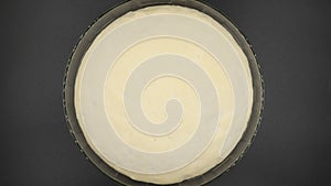 Yeast dough rising in glass bowl on black background, top view