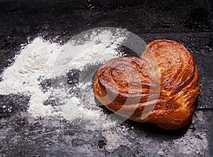 Yeast sweet buns in the shape of a heart on black baking tray. Country house style. Authentically