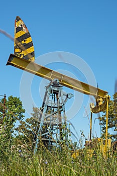 A yellow abandoned oil rig against a background of green grass and blue sky. The concept of the decline of the oil