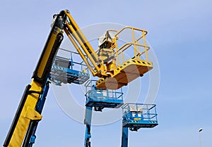 Yellow aerial working platform of cherry picker in front of other three blue.