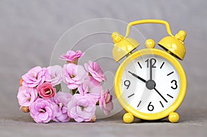 Yellow alarm clock and flowers on grey background