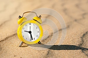 Yellow alarm clock on the sand in the desert on a sunny day with a shadow