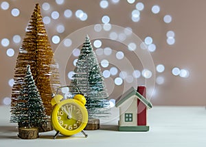 Yellow alarm clock, small house and Christmas trees on the table