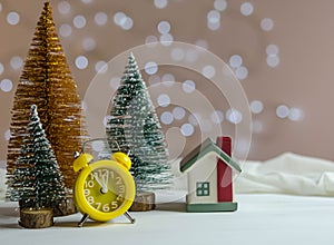 Yellow alarm clock, small house and Christmas trees on the table