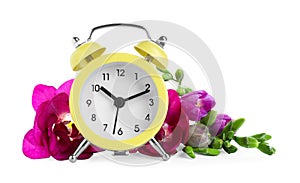 Yellow alarm clock and spring flowers on background. Time change