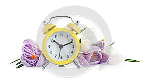 Yellow alarm clock and spring flowers on background. Time change