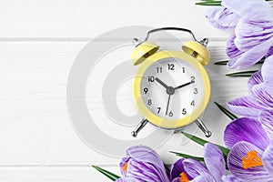 Yellow alarm clock, spring flowers and space for text on white wooden table. Time change