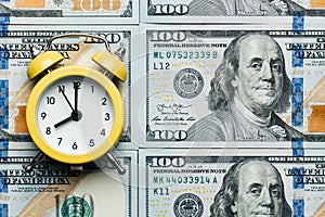 Yellow alarm clock on the stack of one hundred american dollars bills. Credit, deposit and mortgage concept.