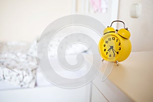 Yellow alarm clock standing on nightstand in background of bed in interior of room. bed`s not made.